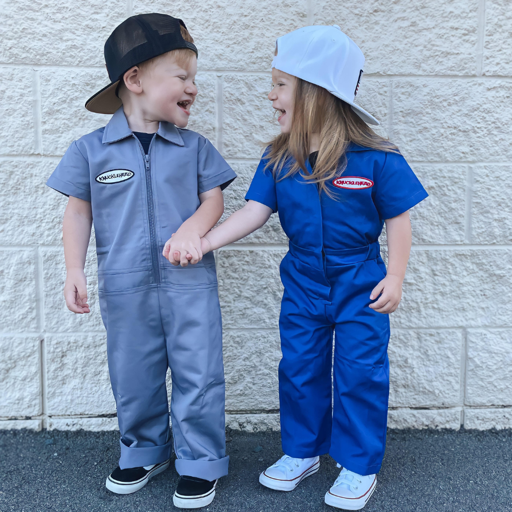 This image showcases delightful baby blue kids' coveralls adorned with a charming Knuckleheads patch, adding a touch of whimsy to your child's wardrobe. These coveralls are not only fashionable but also comfortable, making them an ideal choice for your little one's everyday adventures.