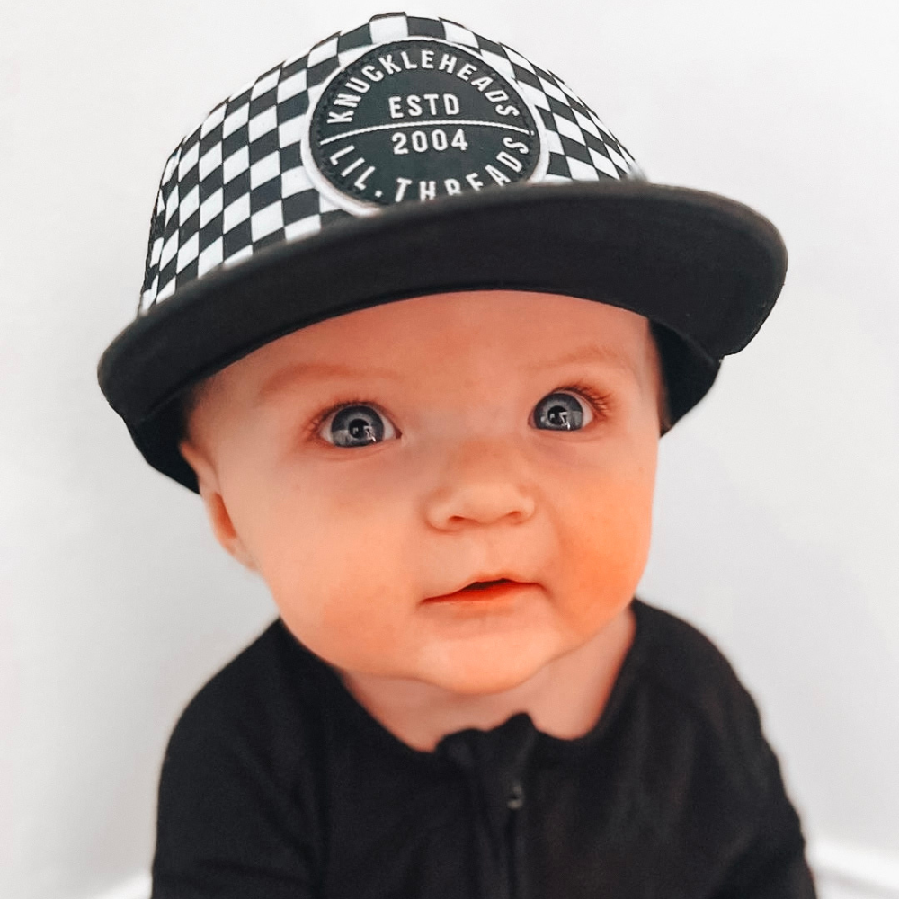 Image of Black and White Checkered Kids Trucker Hat with Knuckleheads Patch: A cool and stylish trucker hat designed for kids. The hat features a trendy black and white checkered pattern, adorned with a striking Knuckleheads patch on the front. Elevate your child's style with this fashionable and eye-catching accessory, perfect for any adventure or everyday wear. Crafted with care, this black and white checkered trucker hat with a Knuckleheads patch is a must-have addition to their wardrobe.
