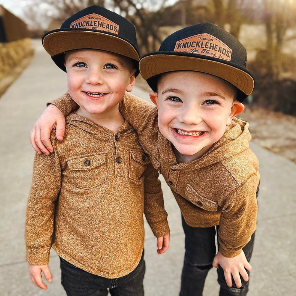Image of Black Kids Trucker Hat with Brown Knuckleheads Patch: A hip and stylish trucker hat designed for kids. The hat comes in sleek black, accentuated with a chic brown Knuckleheads patch on the front. Elevate your child's style with this trendy and versatile accessory, perfect for any adventure or everyday wear. Crafted with comfort in mind, this black trucker hat with a brown patch is a must-have addition to their wardrobe.