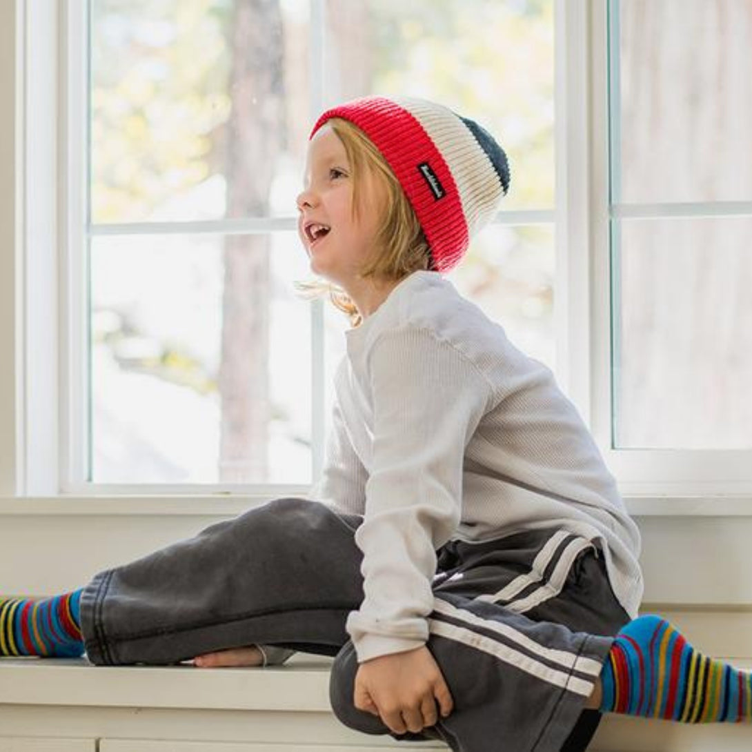 Image featuring a black, white, and red striped beanie from Knuckleheads, crafted for children. This dynamic beanie showcases stylish stripes and includes the Knuckleheads brand tag, suitable for infants and toddlers. An eye-catching addition to the collection of Infant hats, accentuating its charm and appeal.