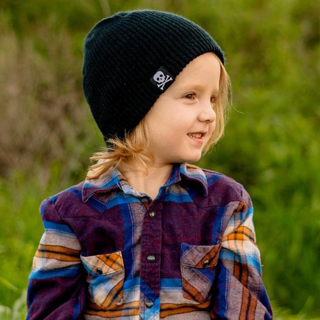 Image featuring a black beanie with a skull tag by Knuckleheads, created for children. This edgy beanie boasts a unique skull tag, adding a touch of style, while remaining suitable for infants and toddlers. A distinctive addition to the collection of Infant hats, infusing a hint of character and charm.
