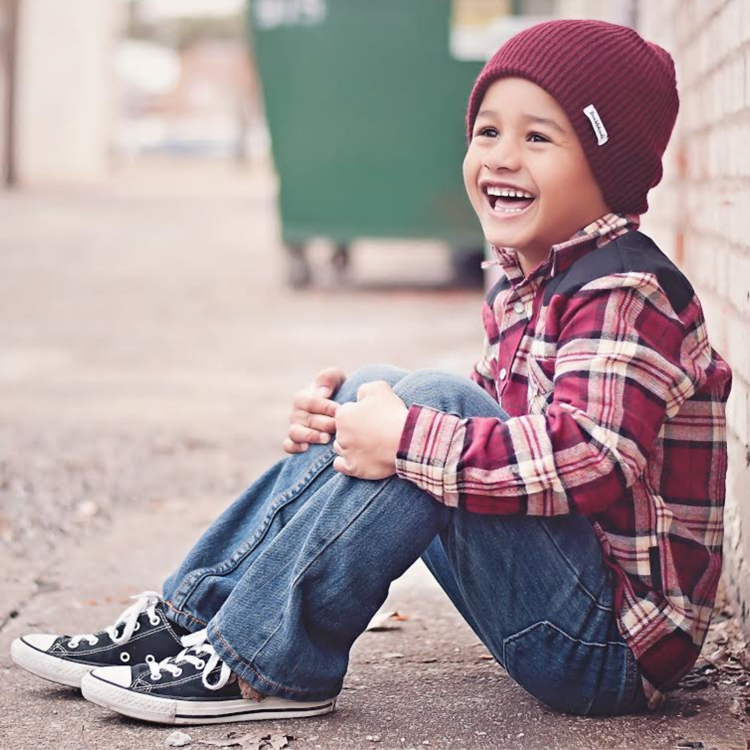 Image of a young boy confidently wearing a Knuckleheads Children's Burgundy Beanie, showcasing its adaptable and cozy design for infants and toddlers. Classic style with the Knuckleheads brand tag. This Toddler beanie is part of a collection of charming Infant hats.