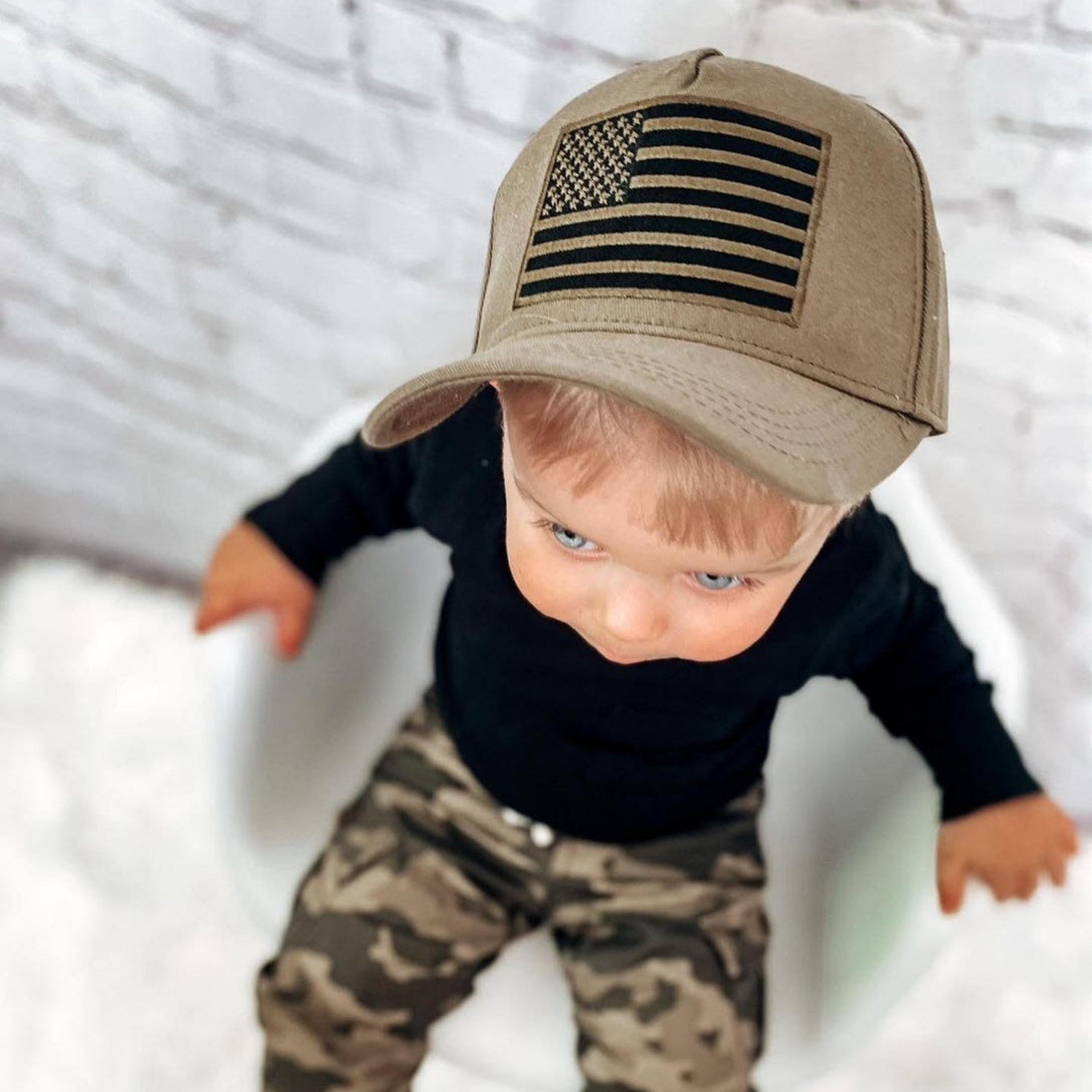 Image of Khaki Kids Trucker Hat with USA Flag Patch: A patriotic and stylish accessory designed for kids. In a versatile khaki shade, it features a prominent USA flag patch on the front. Elevate your child's style with this fashionable hat, perfect for adding a touch of national pride to their outfits.