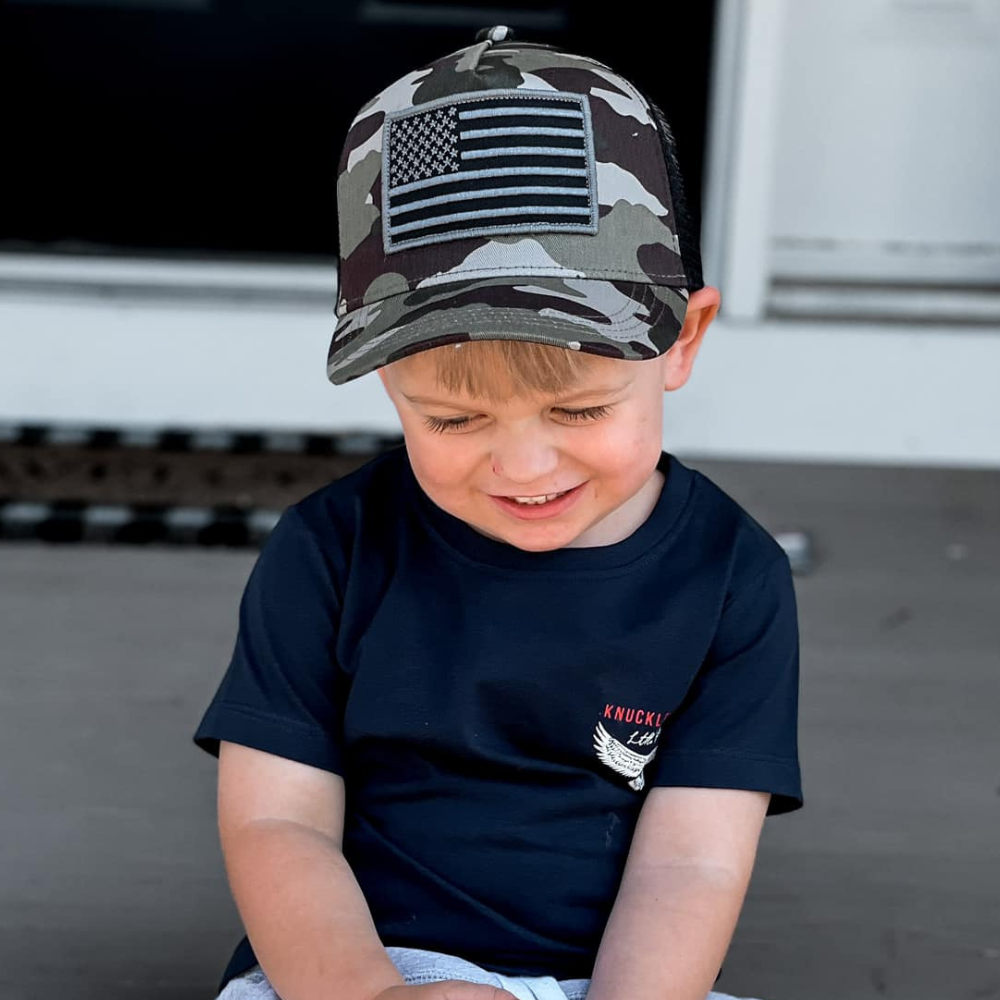 Image of Camo Kids Trucker Hat with USA Flag Patch: A rugged and patriotic accessory designed for kids. In a classic camo pattern, it features a prominent USA flag patch on the front. Elevate your child's style with this fashionable hat, perfect for showcasing their love for the country. Crafted with care, this camo kids trucker hat with the USA flag patch is a must-have addition to their wardrobe, suitable for various occasions and everyday wear.