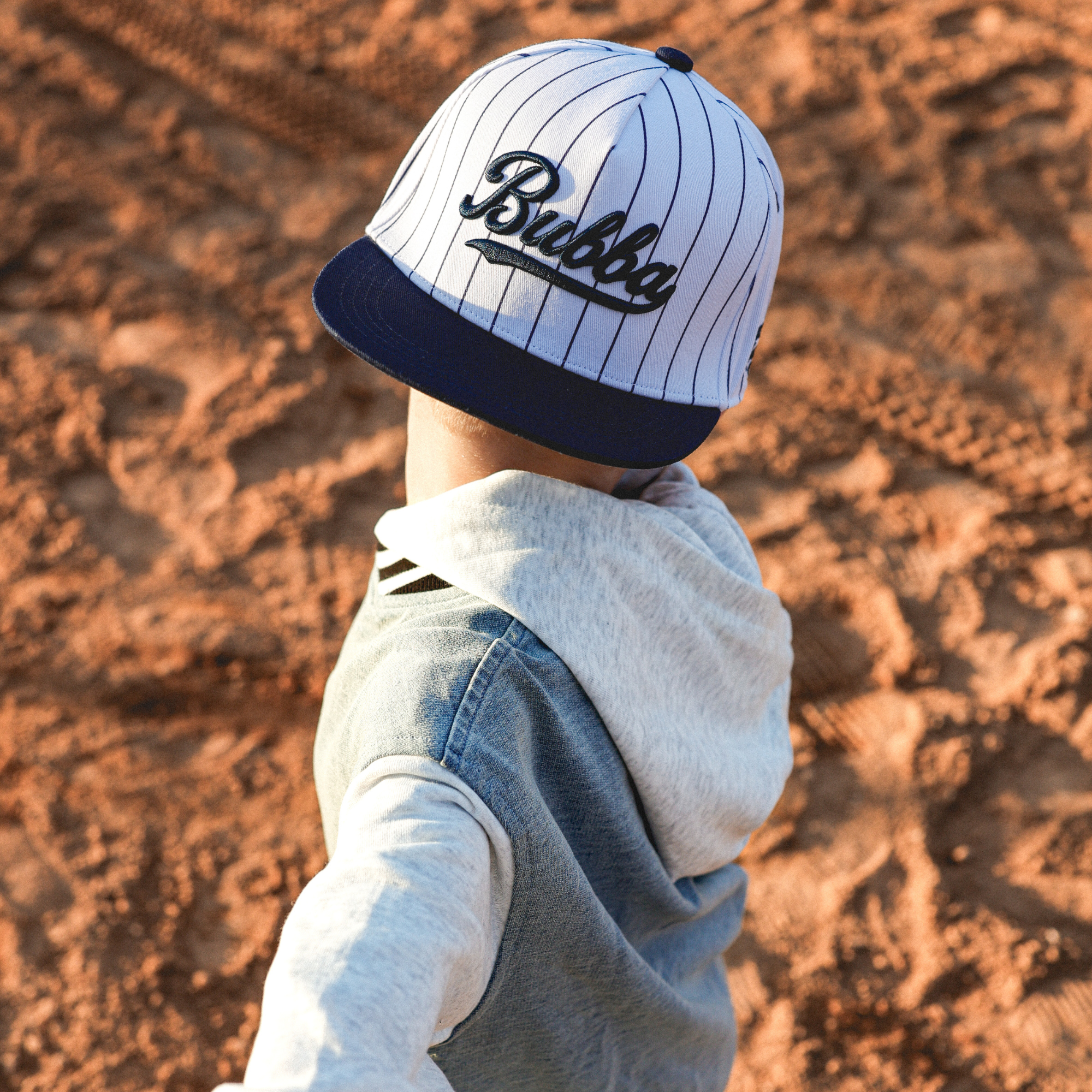 Lifestyle photo of toddler wearing Bubba embroidered snapback hat with navy pinstripes outdoors