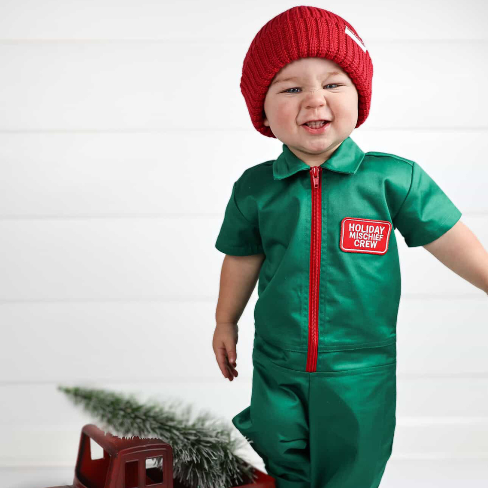 Holiday-themed toddler coverall in bright green with a red zipper and “Holiday Mischief Crew” patch, giving a playful mechanic look perfect for Christmas photos and adventures