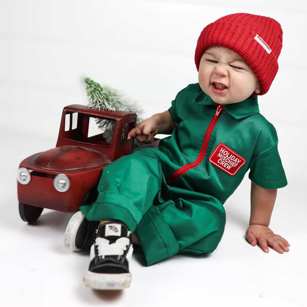 Holiday-themed toddler coverall in bright green with a red zipper and “Holiday Mischief Crew” patch, giving a playful mechanic look perfect for Christmas photos and adventures