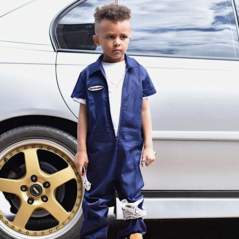 This image showcases delightful navy kids' coveralls adorned with a charming Knuckleheads patch, adding a touch of whimsy to your child's wardrobe. These coveralls are not only fashionable but also comfortable, making them an ideal choice for your little one's everyday adventures.