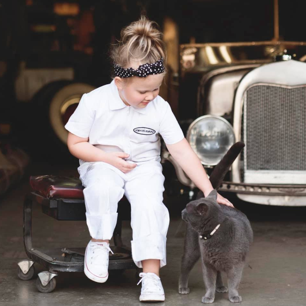 This image showcases delightful white kids' coveralls adorned with a charming Knuckleheads patch, adding a touch of whimsy to your child's wardrobe. These coveralls are not only fashionable but also comfortable, making them an ideal choice for your little one's everyday adventures.