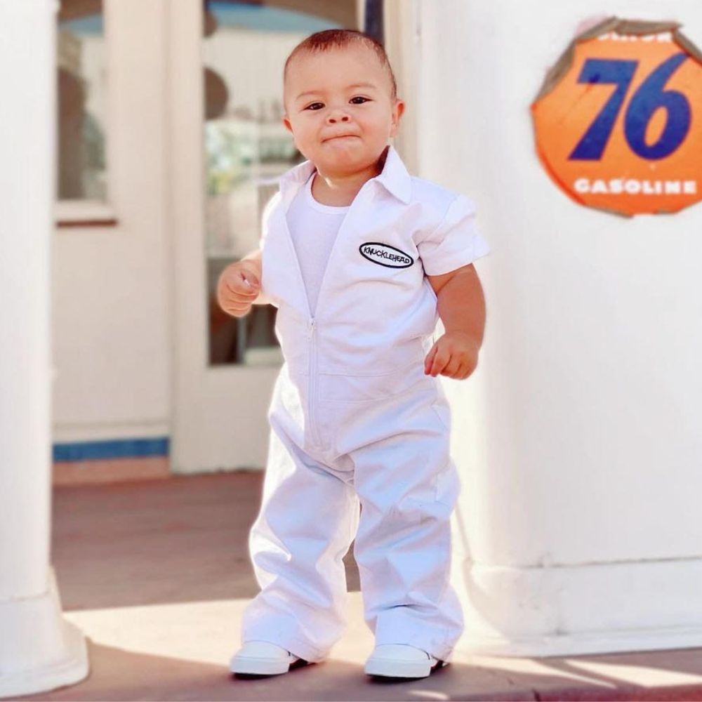 This image showcases delightful white kids' coveralls adorned with a charming Knuckleheads patch, adding a touch of whimsy to your child's wardrobe. These coveralls are not only fashionable but also comfortable, making them an ideal choice for your little one's everyday adventures.