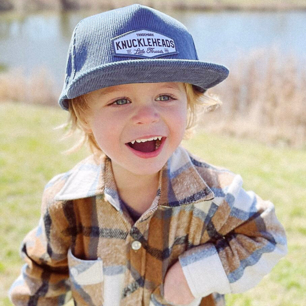 Image of Blue Corduroy Kids Trucker Hat with Knuckleheads Patch: A vintage-inspired and stylish accessory designed for kids. In a rich blue corduroy fabric, it showcases a striking Knuckleheads patch on the front. Elevate your child's style with this fashionable hat, perfect for adding a touch of texture to their outfits. 