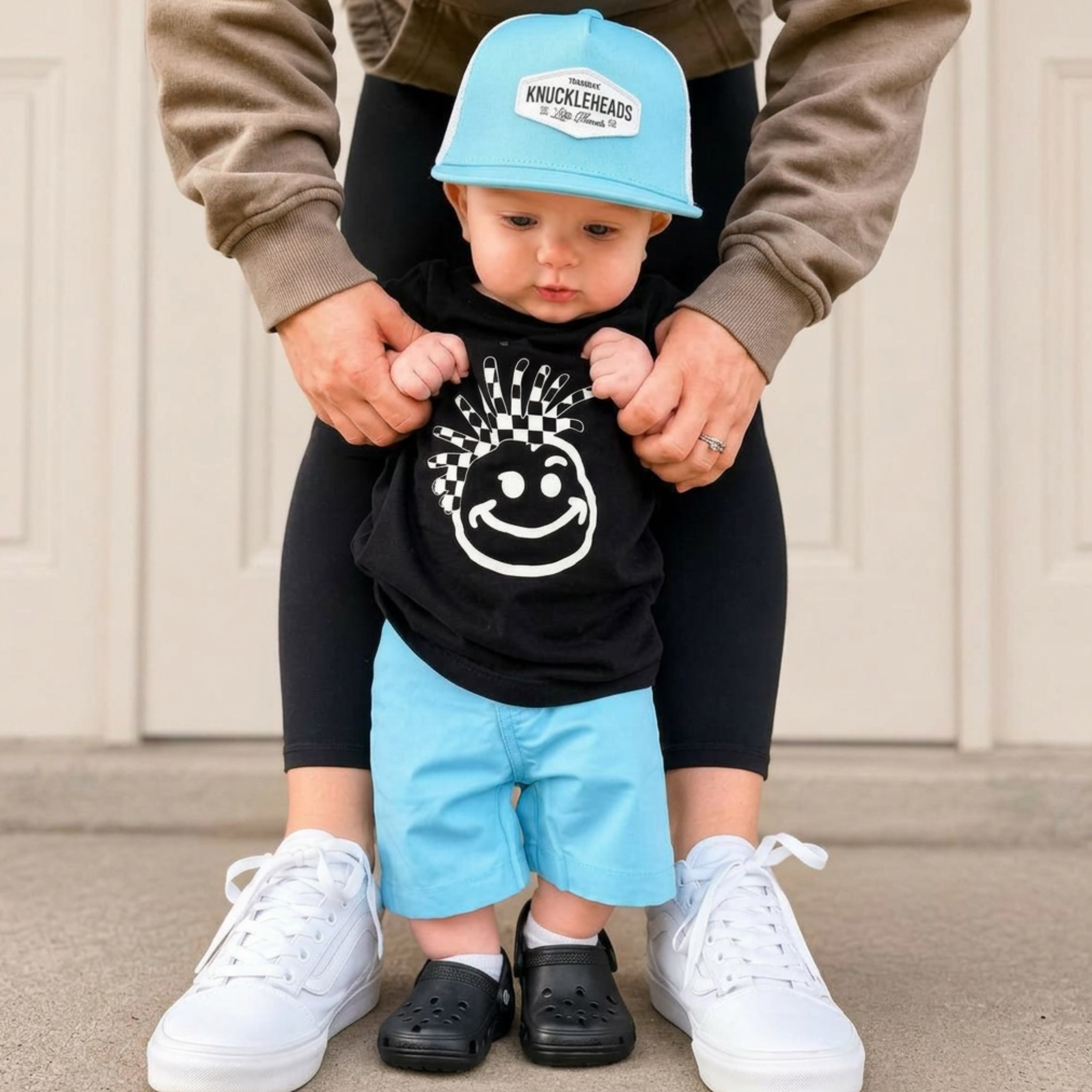 Baby modeling the Colt Infant Trucker Hat, a light blue and white beach-style trucker hat for infants, while learning to walk outdoors.