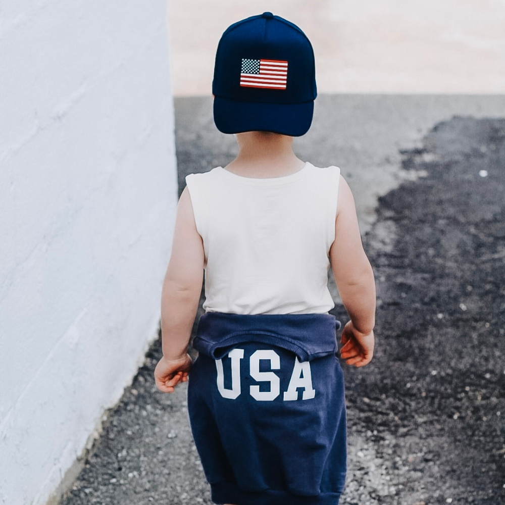 Image of Navy USA Kids Trucker Hat with USA Flag Patch: A patriotic and stylish trucker hat designed for kids. The hat comes in classic navy blue, showcasing a striking USA flag patch on the front. Perfect for young patriots to show their American pride while staying cool and comfortable. Elevate your child's style with this trendy and functional accessory, ideal for outdoor adventures and everyday wear.