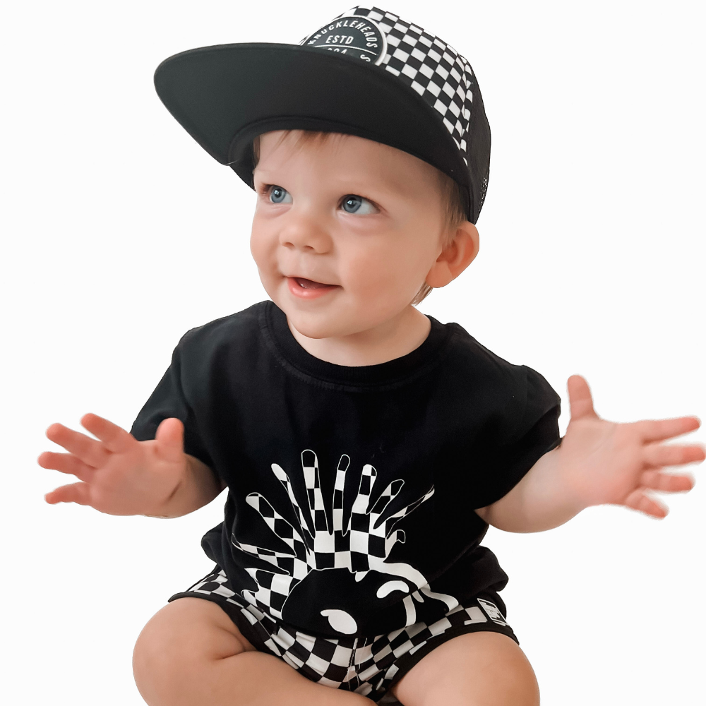 Image of Black Kids T-Shirt with Checkered Knuckleheads Logo: A cool and trendy wardrobe addition for kids. In classic black, it boasts a stylish checkered Knuckleheads logo on the front. Elevate your child's style with this fashionable t-shirt, perfect for adding a touch of edgy flair to their outfits. Crafted with care, this black kids t-shirt with the checkered Knuckleheads logo is a must-have piece, suitable for various occasions and everyday wear.