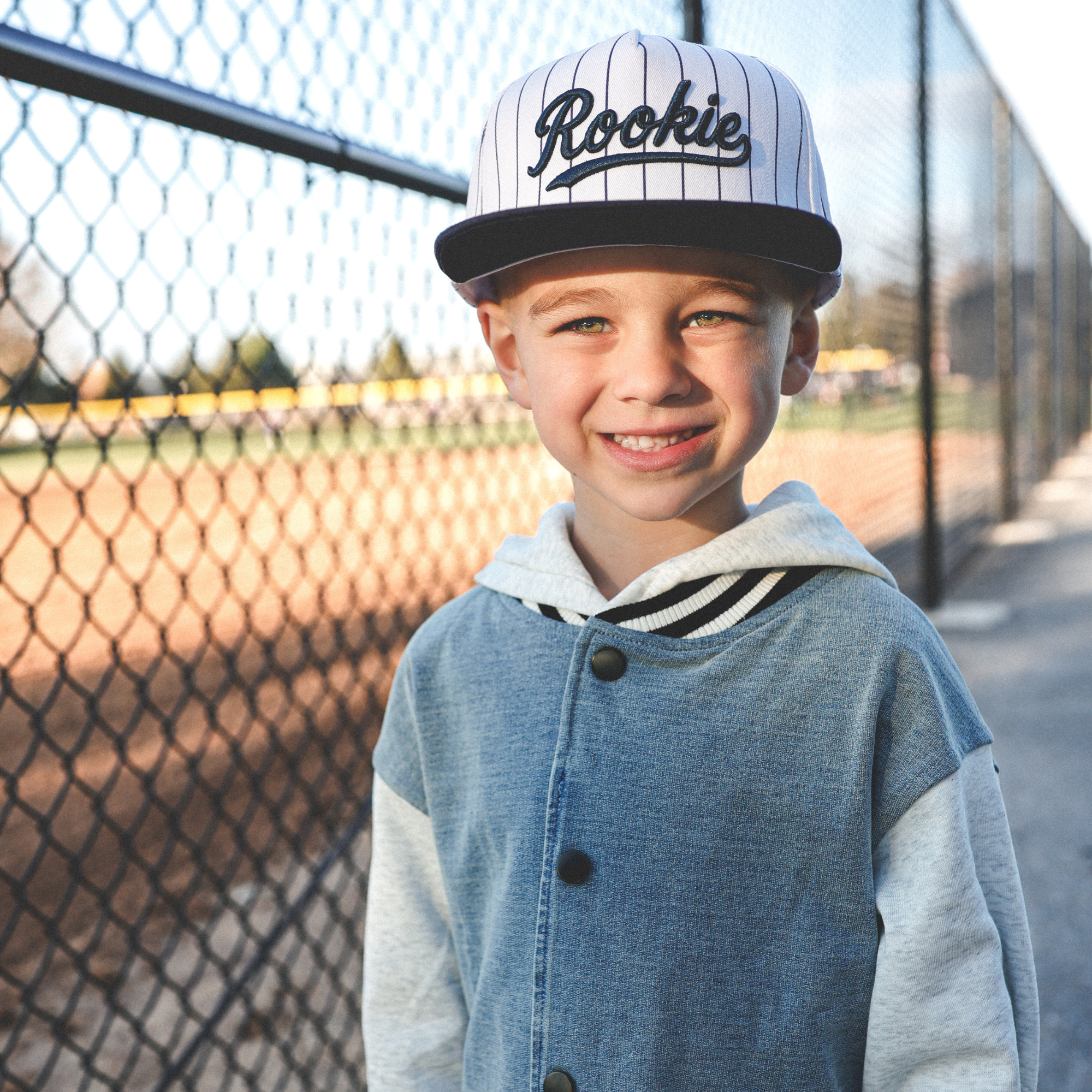 Lifestyle photo of toddler wearing Rookie snapback hat with navy pinstripes at baseball field