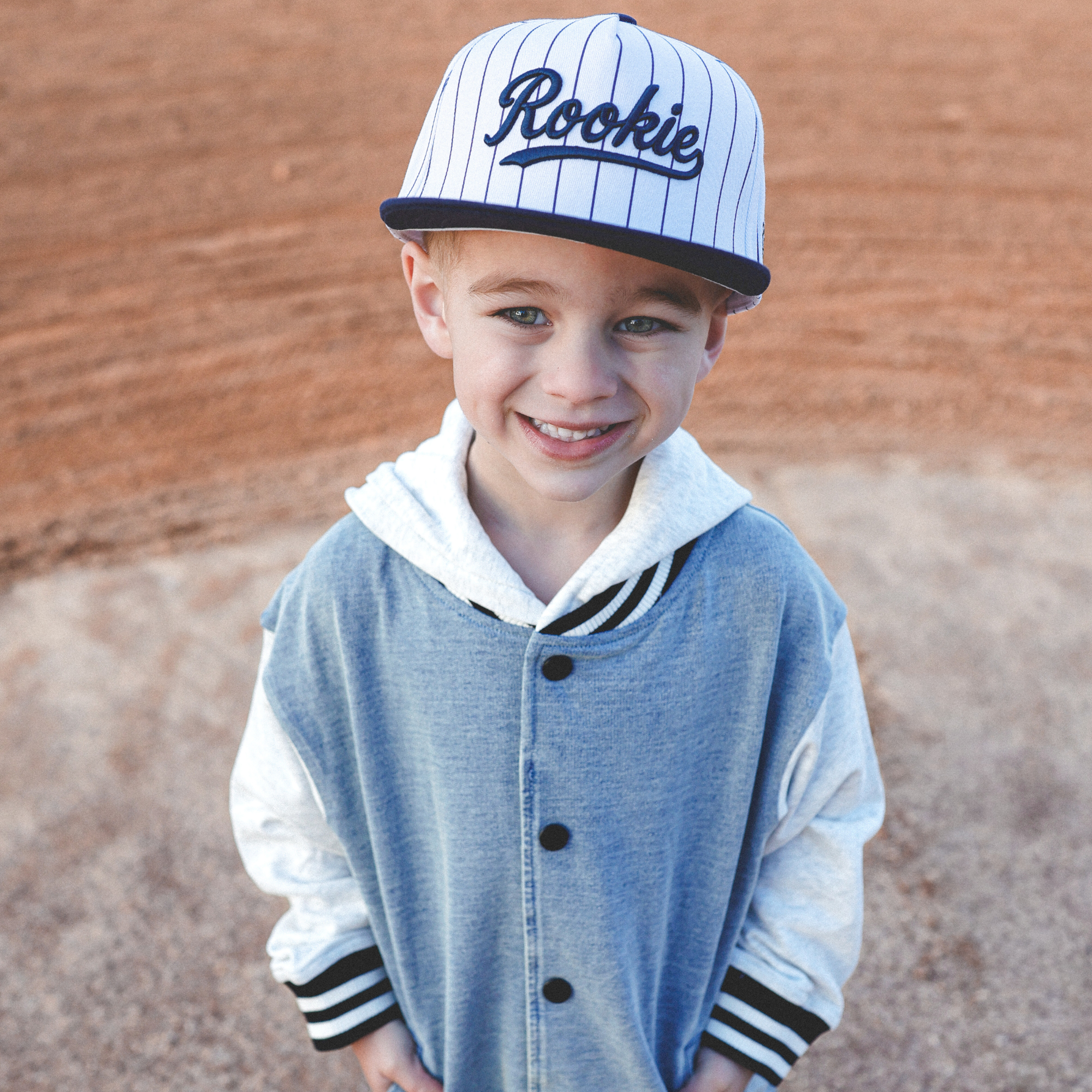 Lifestyle photo of toddler wearing Rookie snapback hat with navy pinstripes at baseball field