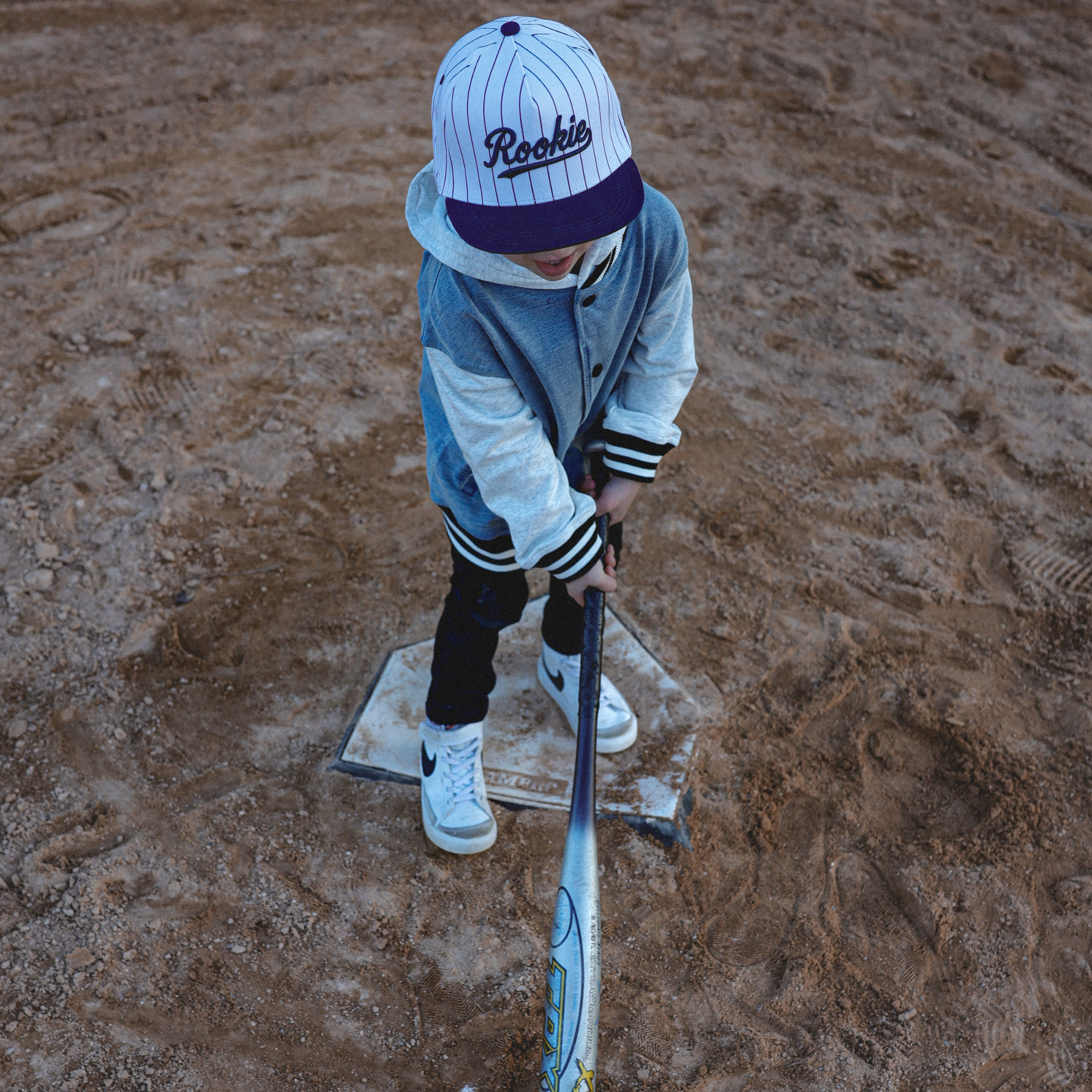 Lifestyle photo of toddler wearing Rookie snapback hat with navy pinstripes at baseball field