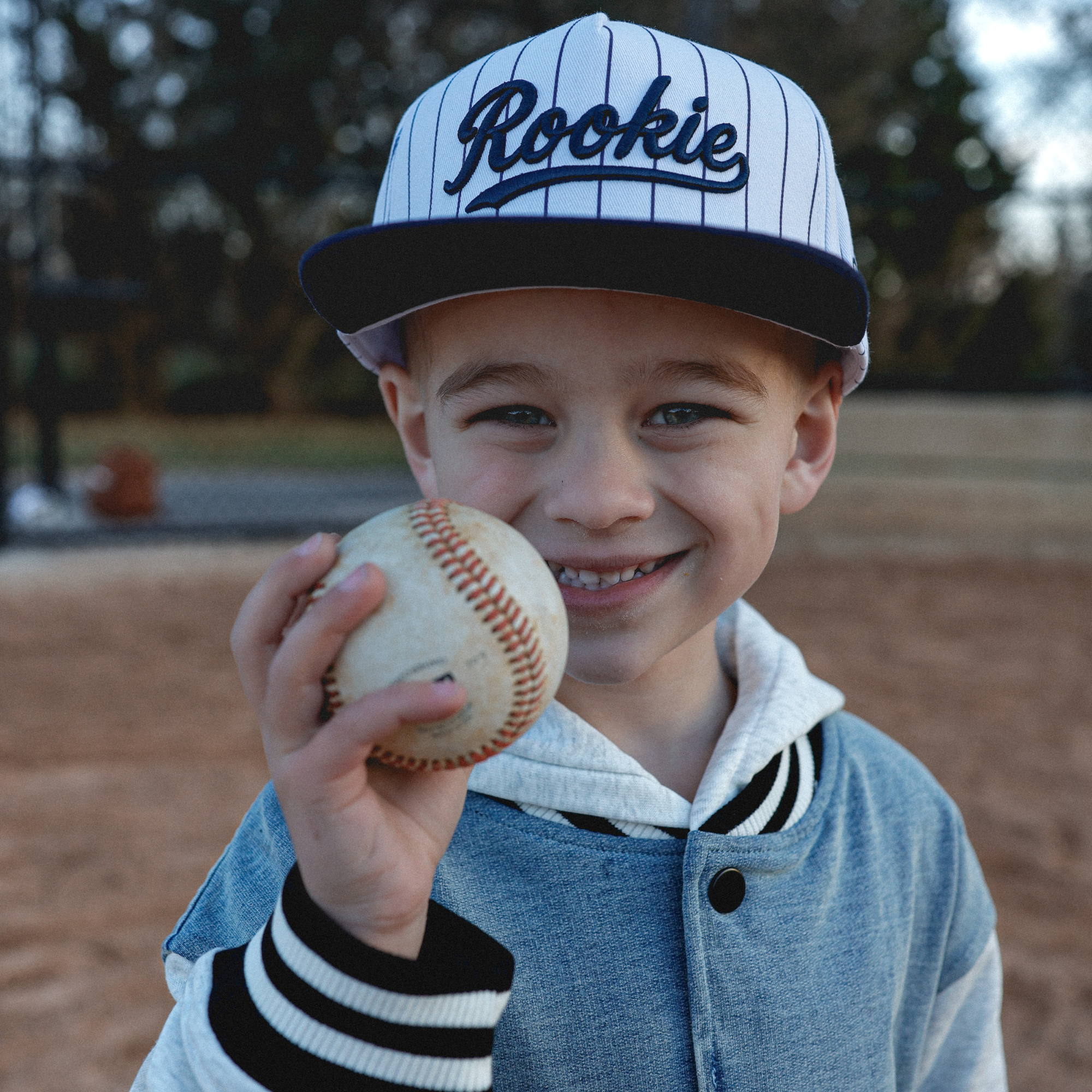 Lifestyle photo of toddler wearing Rookie snapback hat with navy pinstripes at baseball field