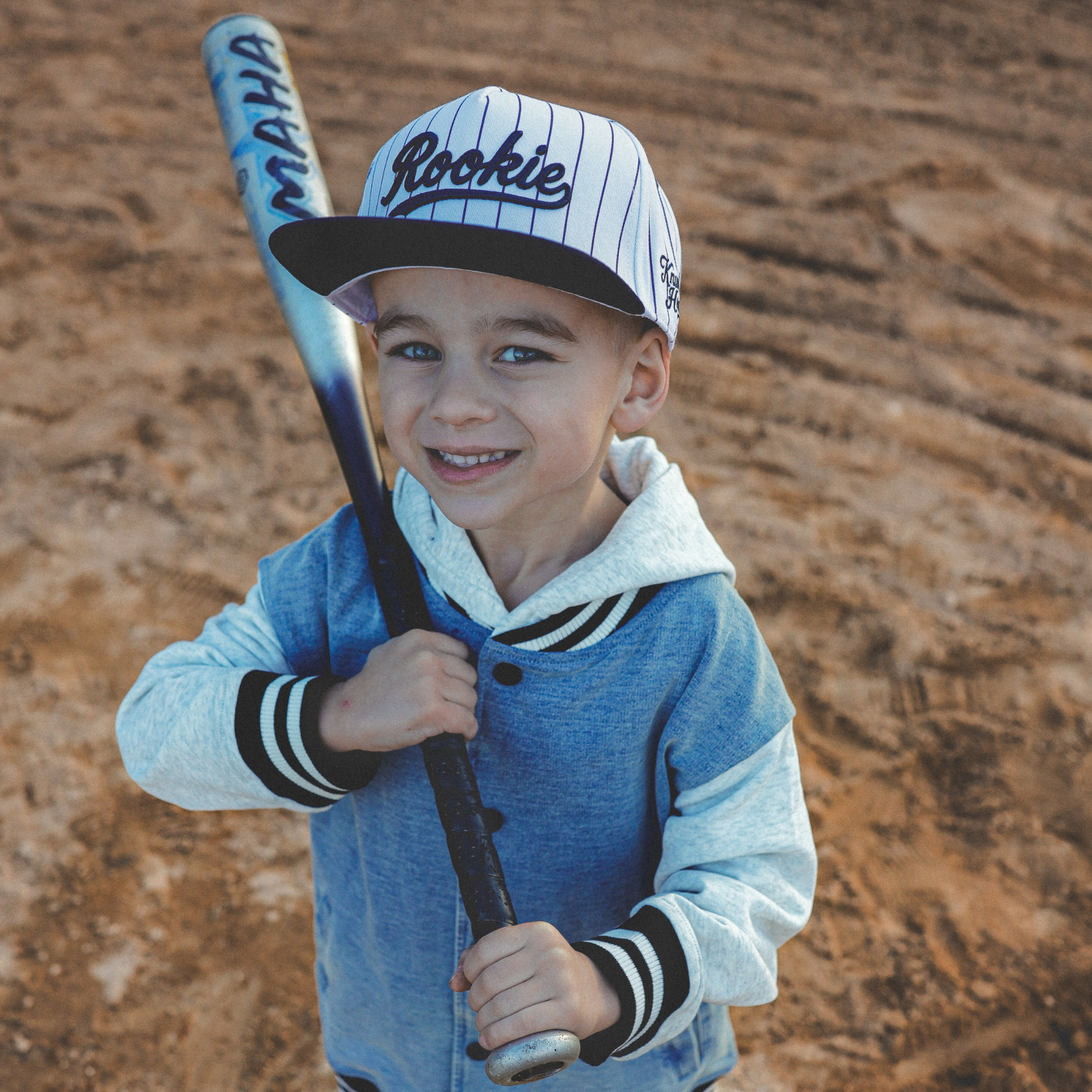 Lifestyle photo of toddler wearing Rookie snapback hat with navy pinstripes at baseball field
