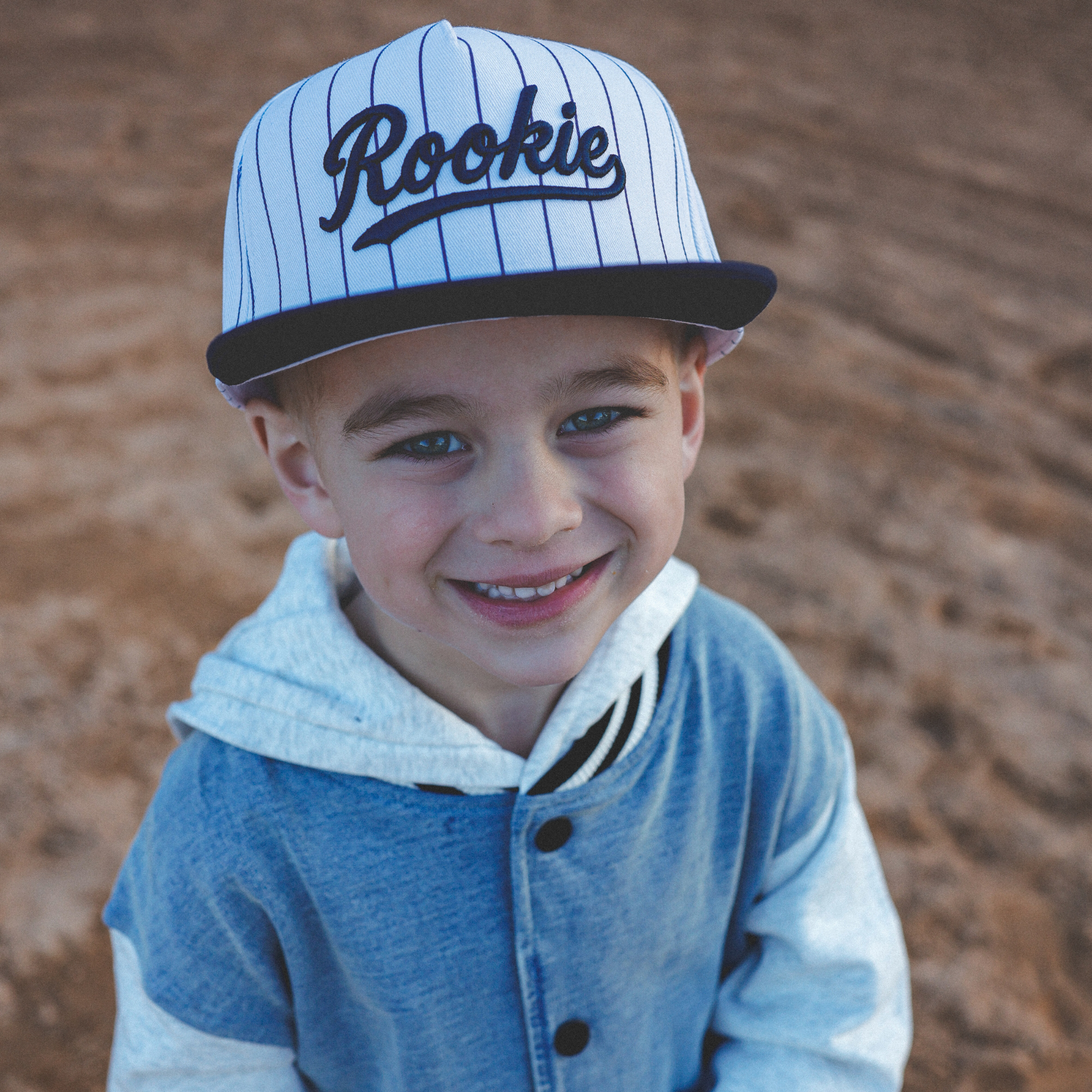 Lifestyle photo of toddler wearing Rookie snapback hat with navy pinstripes at baseball field