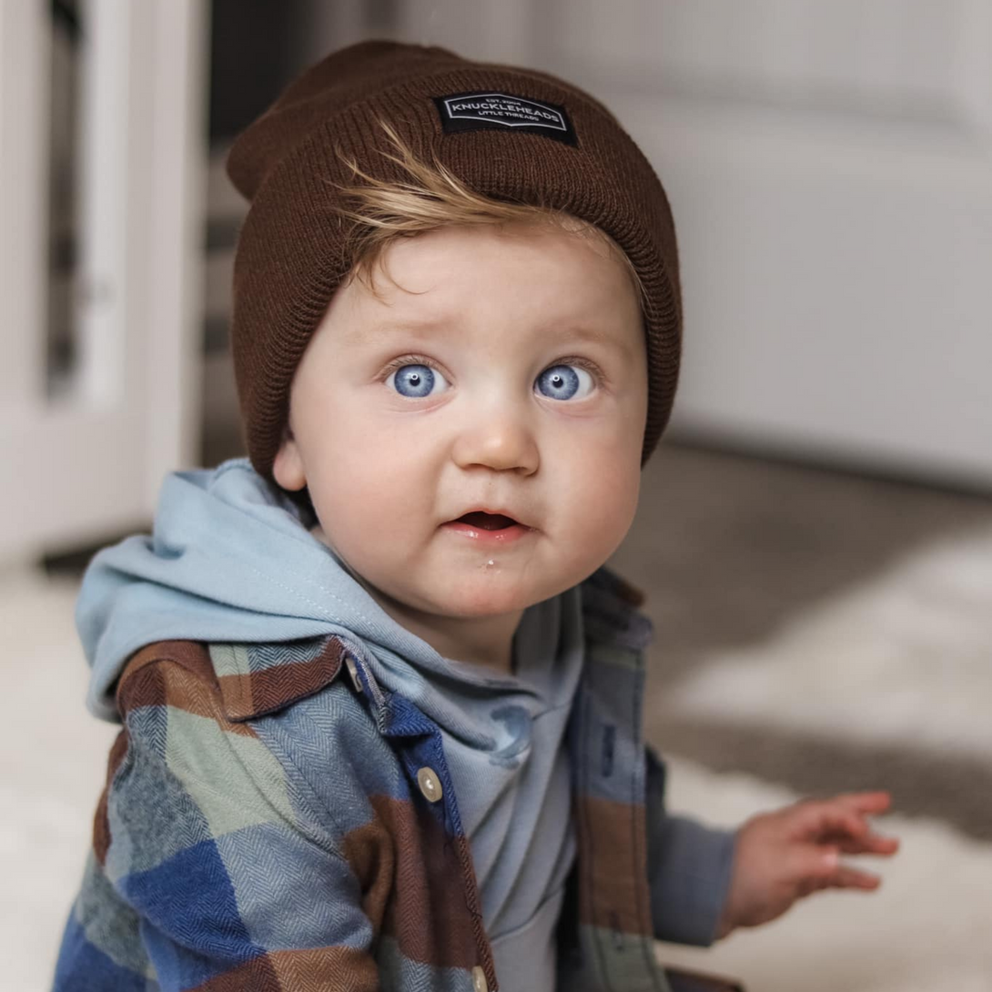 Image of Brown Kids Beanie with Knuckleheads Logo: This green beanie is both stylish and cozy for kids. The Knuckleheads logo on the front adds a unique touch to their outfits while keeping them warm. Crafted with care, this beanie is a versatile addition to their winter wardrobe, suitable for various occasions and everyday wear.