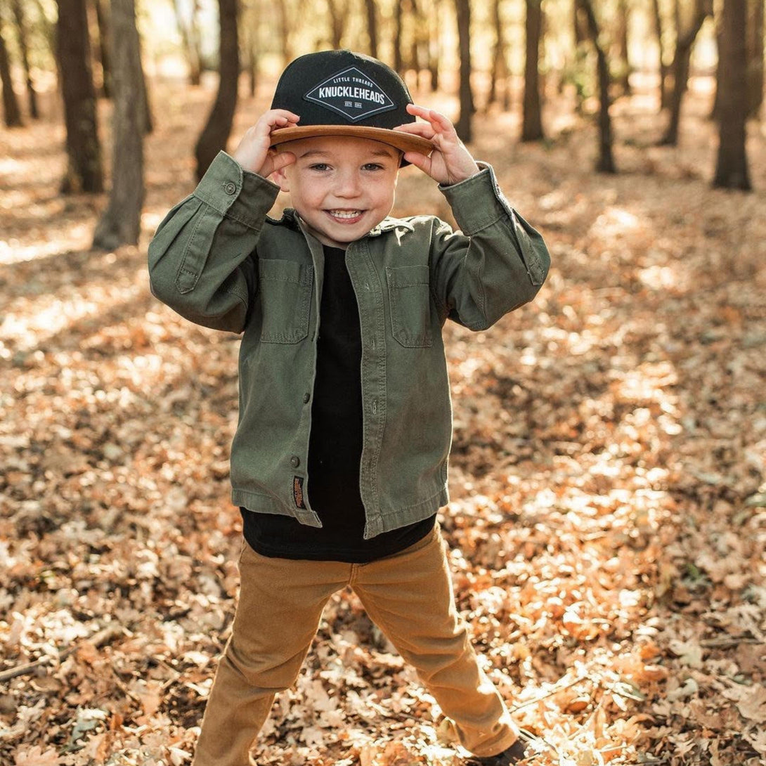 Image of Black and Brown Kids Trucker Hat with Knuckleheads Patch: A stylish and versatile accessory designed for kids. Combining sleek black and warm brown tones, it features a striking Knuckleheads patch on the front. Elevate your child's style with this fashionable hat, perfect for adding a touch of contrast to their outfits.