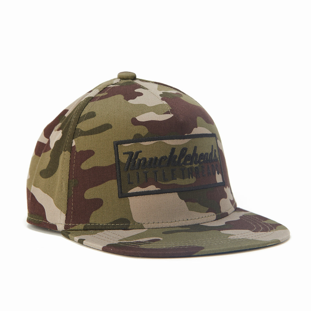 Image of Camo Kids Trucker Hat with Black Rectangle Knuckleheads Patch: A rugged and stylish accessory designed for kids. In a classic camo pattern, it features a bold black rectangle Knuckleheads patch on the front. Elevate your child's style with this fashionable hat, perfect for adding a touch of outdoor charm to their outfits.
