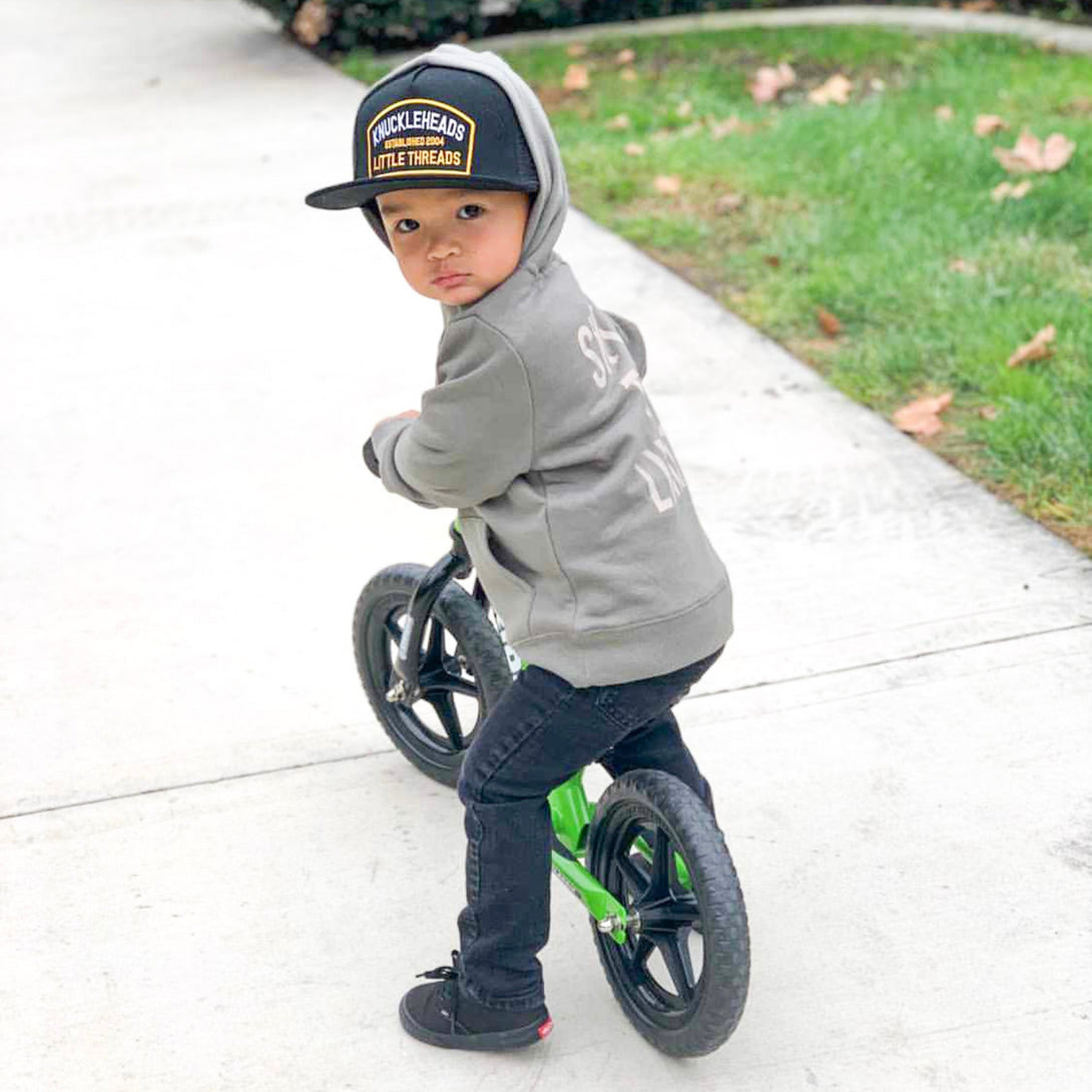 Image of Black Kids Trucker Hat with Black Mesh and Knuckleheads Patch: A sleek and stylish accessory designed for kids. In classic black with matching black mesh, it showcases a striking Knuckleheads patch on the front. Elevate your child's style with this fashionable hat, perfect for adding a touch of edgy flair to their outfits while ensuring breathability. 