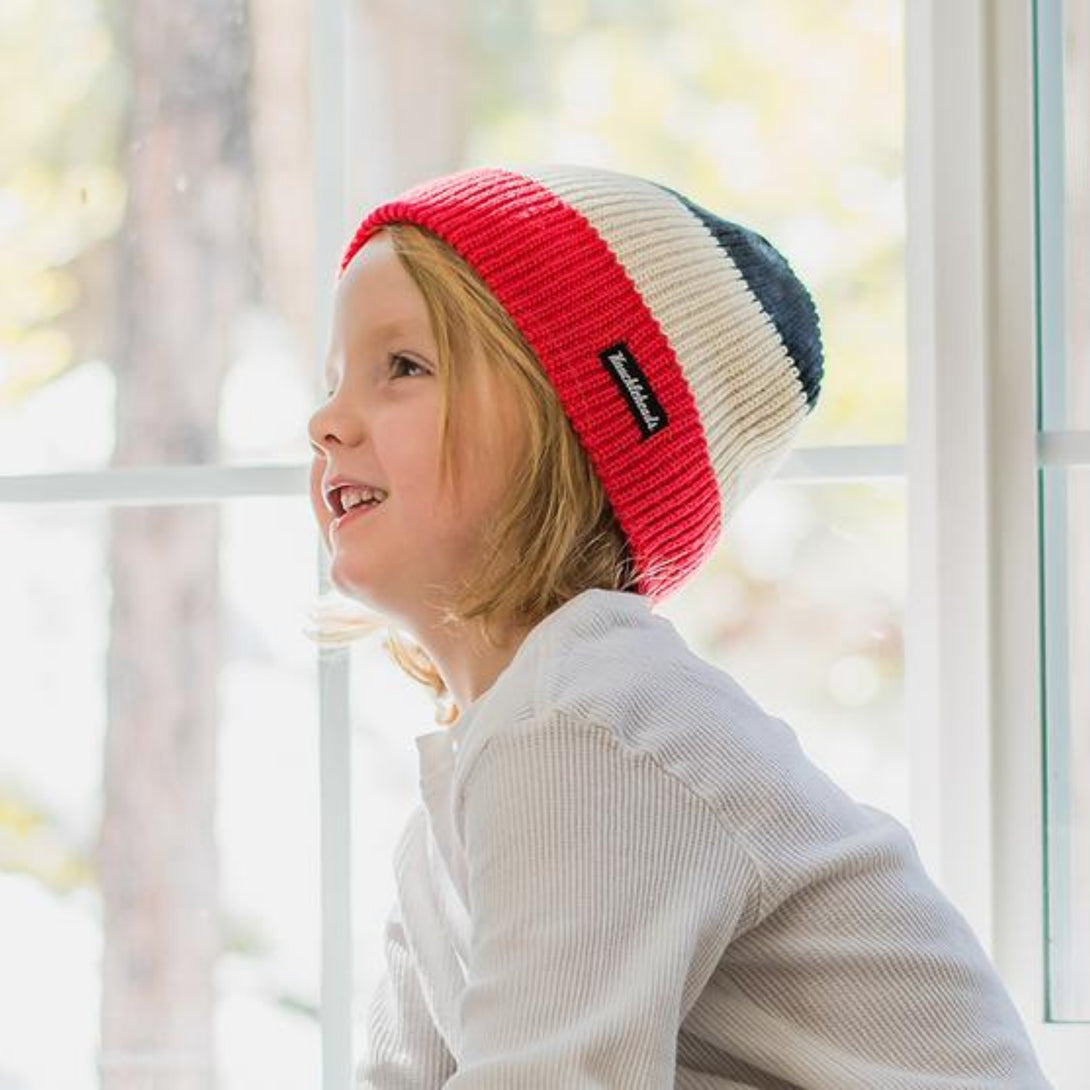 Image featuring a black, white, and red striped beanie from Knuckleheads, crafted for children. This dynamic beanie showcases stylish stripes and includes the Knuckleheads brand tag, suitable for infants and toddlers. An eye-catching addition to the collection of Infant hats, accentuating its charm and appeal.