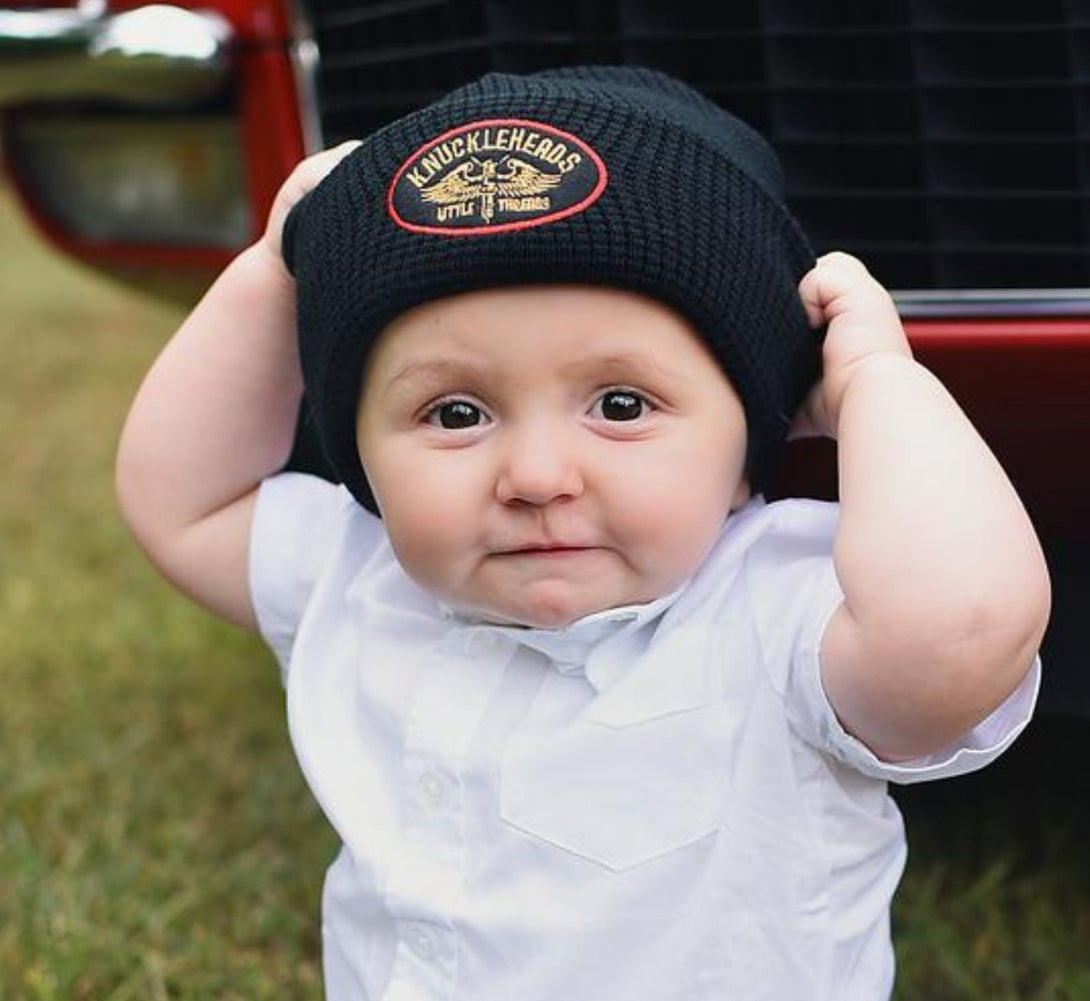 Image of a young boy wearing a black Knuckleheads beanie with the classic brand tag. The stylish beanie adds a touch of urban flair to the boy's outfit, showcasing his individuality and confidence.
