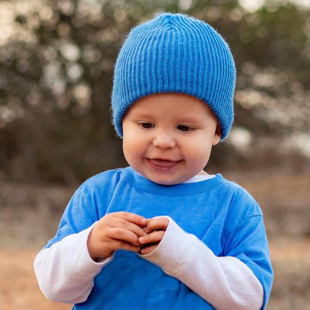 Image of a young boy wearing a children's blue Baby Beanie by Knuckleheads, showcasing its versatile and comfortable design for infants and toddlers. Classic style with Knuckleheads brand tag. This Toddler beanie is part of a collection of charming Infant hats.