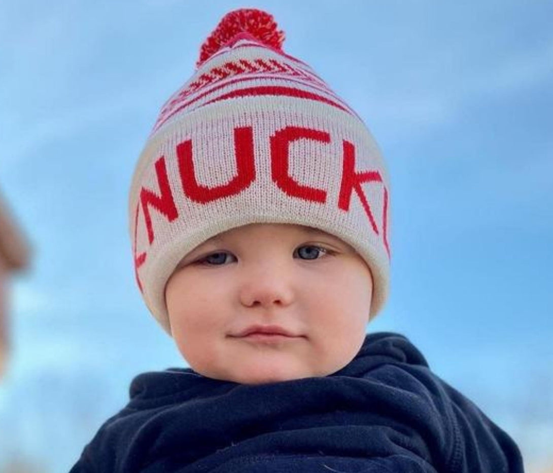 Image displaying a red and white fold-up beanie with a pom from Knuckleheads, designed for children. This versatile beanie combines a classic style with the Knuckleheads brand tag, perfect for infants and toddlers. A playful addition to the collection of Infant hats, enhancing its charm.