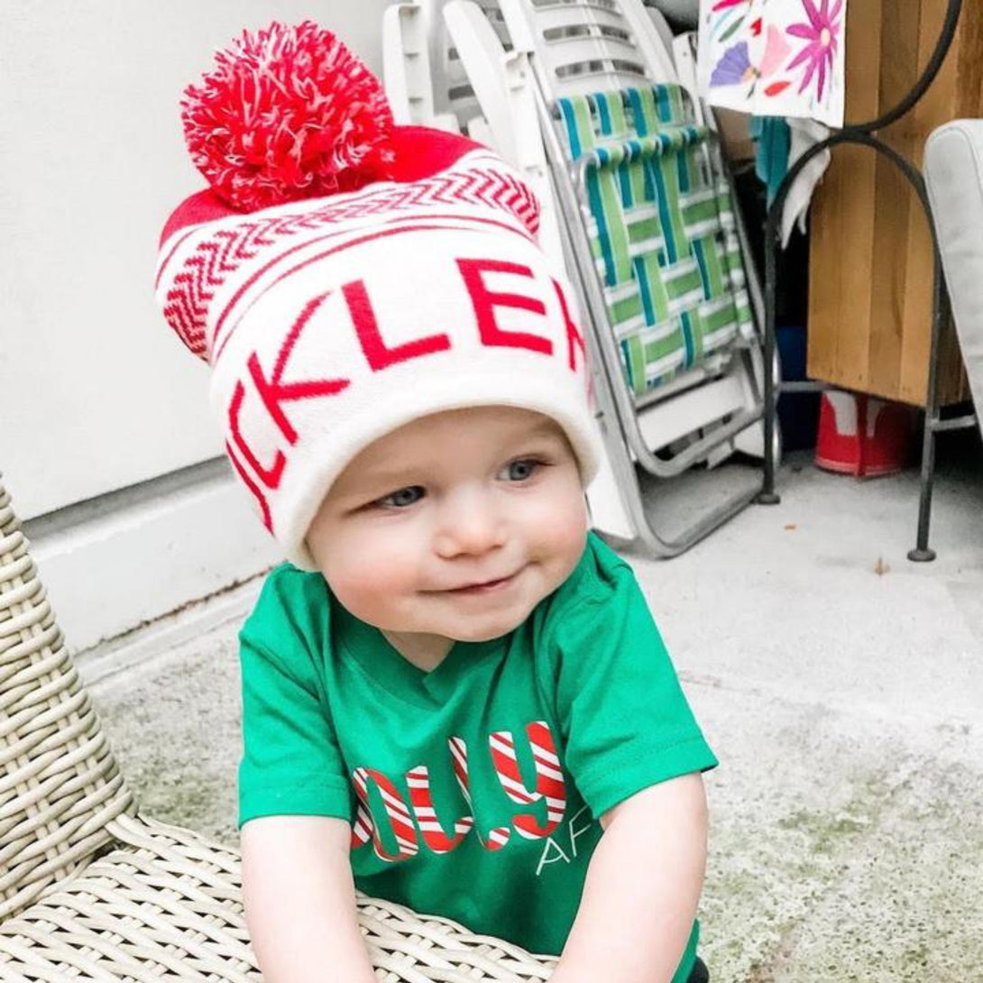 Image displaying a red and white fold-up beanie with a pom from Knuckleheads, designed for children. This versatile beanie combines a classic style with the Knuckleheads brand tag, perfect for infants and toddlers. A playful addition to the collection of Infant hats, enhancing its charm.