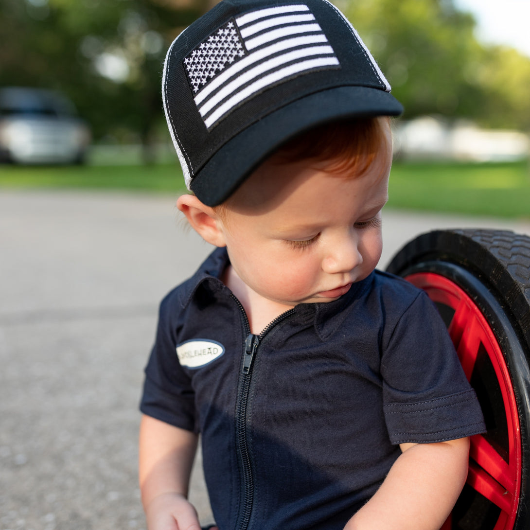 Image of Black Kids Trucker Hat with White Mesh and USA Flag Patch: A patriotic and stylish accessory designed for kids. In deep navy with crisp white mesh, it features a prominent USA flag patch on the front. Elevate your child's style with this fashionable hat, perfect for adding a touch of national pride to their outfits while ensuring breathability.
