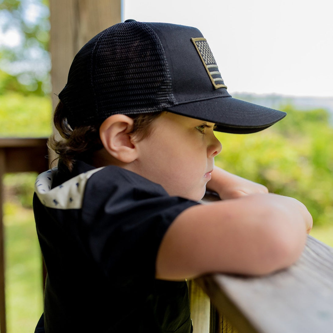 Image of Black Kids Trucker Hat with USA Flag Patch: A patriotic and stylish accessory designed for kids. In classic black, it features a prominent USA flag patch on the front. Elevate your child's style with this fashionable hat, perfect for adding a touch of national pride to their outfits.