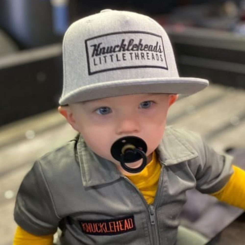 Image of Grey Kids Trucker Hat with Black Mesh and Knuckleheads Patch: A modern and stylish accessory designed for kids. In sleek grey with contrasting black mesh, it features a striking Knuckleheads patch on the front. Elevate your child's style with this fashionable hat, perfect for adding a touch of contrast to their outfits while ensuring breathability.