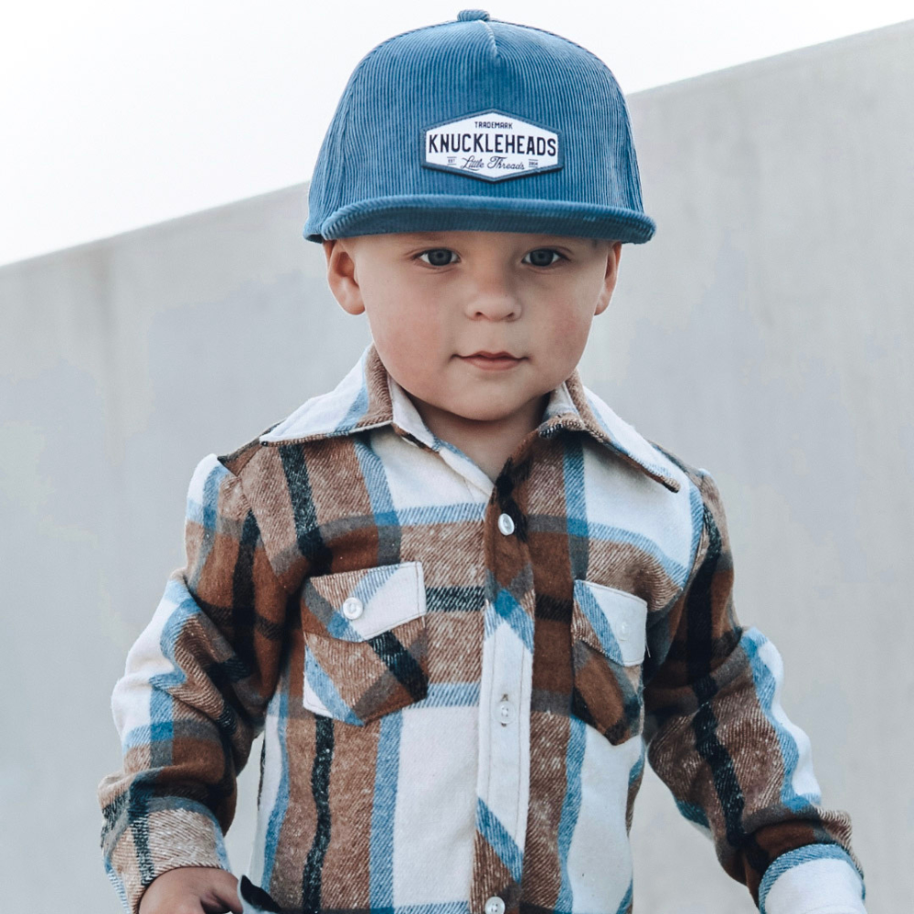 Image of Blue Corduroy Kids Trucker Hat with Knuckleheads Patch: A vintage-inspired and stylish accessory designed for kids. In a rich blue corduroy fabric, it showcases a striking Knuckleheads patch on the front. Elevate your child's style with this fashionable hat, perfect for adding a touch of texture to their outfits. 