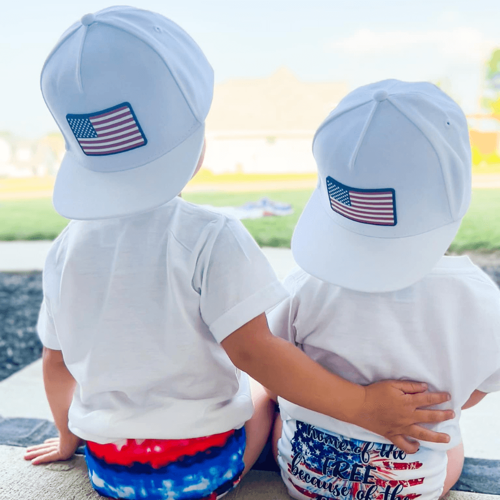 Image of White Trucker Hat for Kids with USA Flag Patch: A patriotic and stylish accessory designed for kids. In classic white, it showcases a prominent USA flag patch on the front. Elevate your child's style with this fashionable hat, perfect for showing their national pride. Crafted with care, this white kids trucker hat with the USA flag patch is a must-have addition to their wardrobe, suitable for various occasions and everyday wear.
